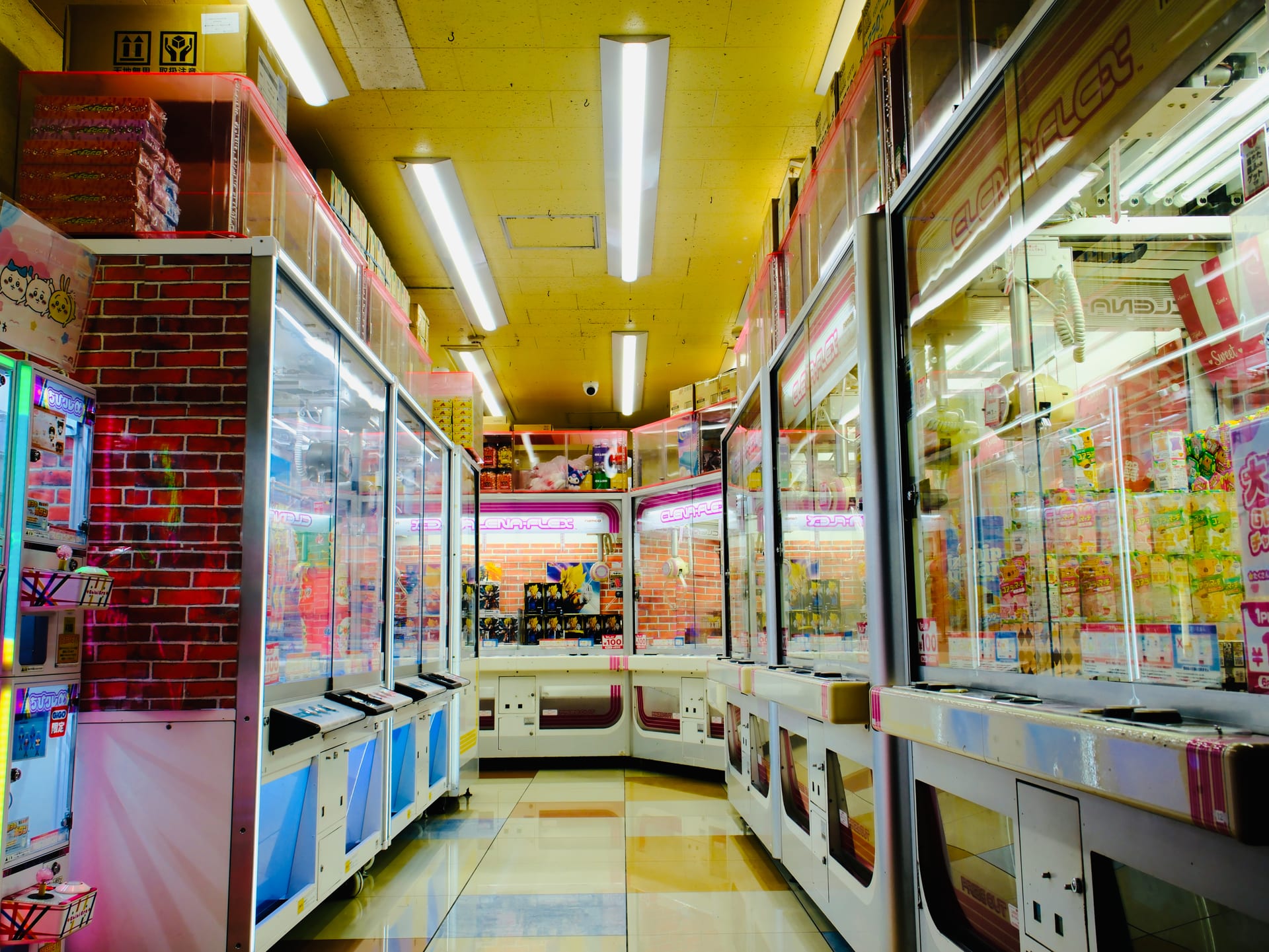 An empty arcade corridor of claw machines under yellow light.
